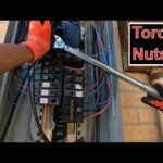 A person with red gloves is using a torque wrench on a breaker box with exposed wires and electrical components. The text Torque Nuts is displayed at the top right.